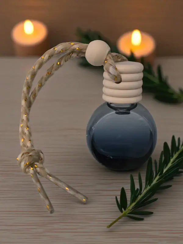 Glass rosemary car diffuser with wooden cap, styled with rosemary sprigs and candles on a light wood surface from Homestead Lavender Farm.