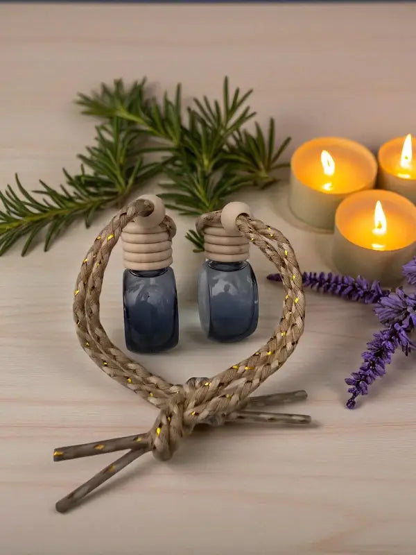 Glass rosemary car diffuser with wooden cap, styled with rosemary sprigs and lavender with candles on a light wood surface from Homestead Lavender Farm.