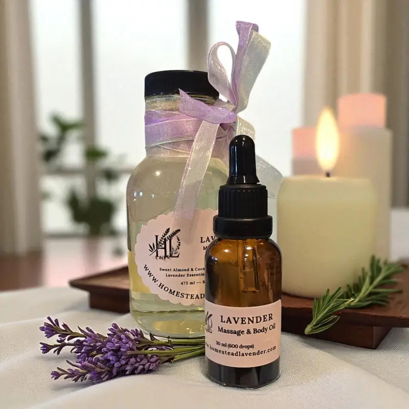 An 8 fl oz clear glass and 30ml amber glass vial of lavender massage oil with candles and sprigs of lrosemary and lavender