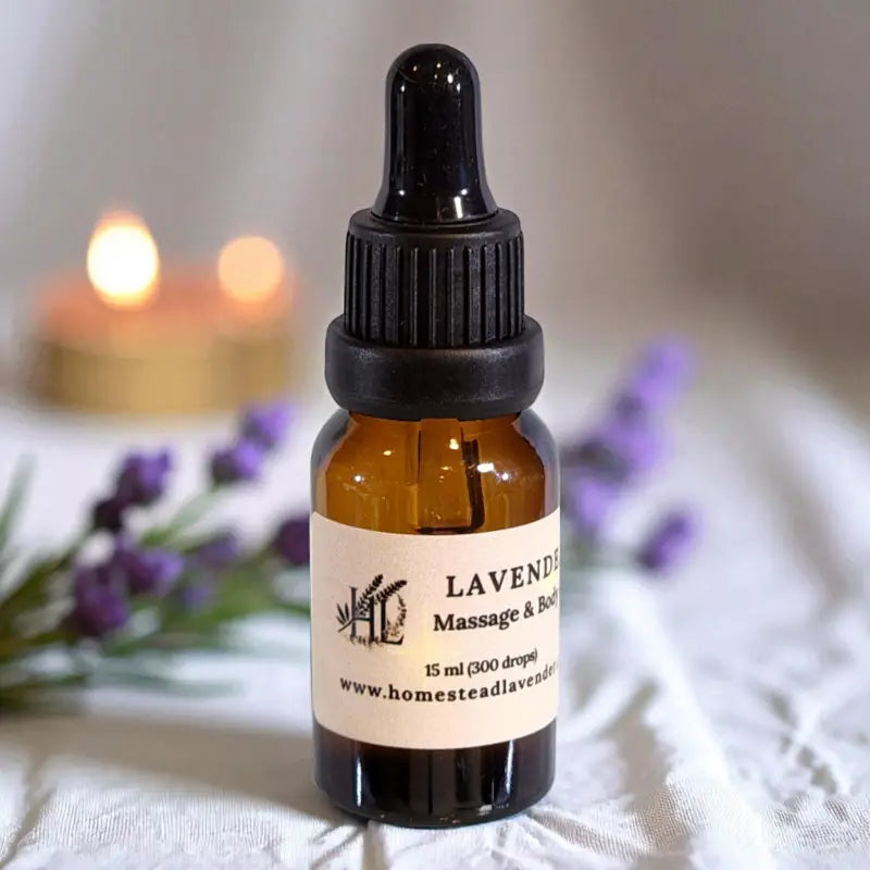 A 15ml dropper bottle of lavender massage oil with candles and sprigs of lavender