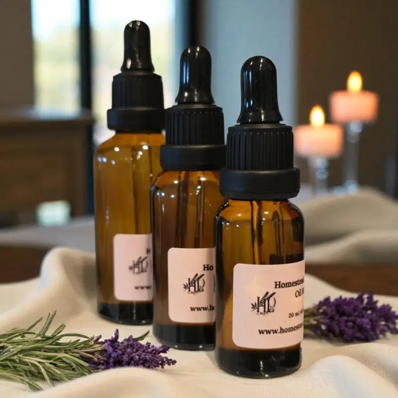 Three amber glass bottles with black dropper lids of massage oil on a cloth with lavender and rosemary, candles in the background.
