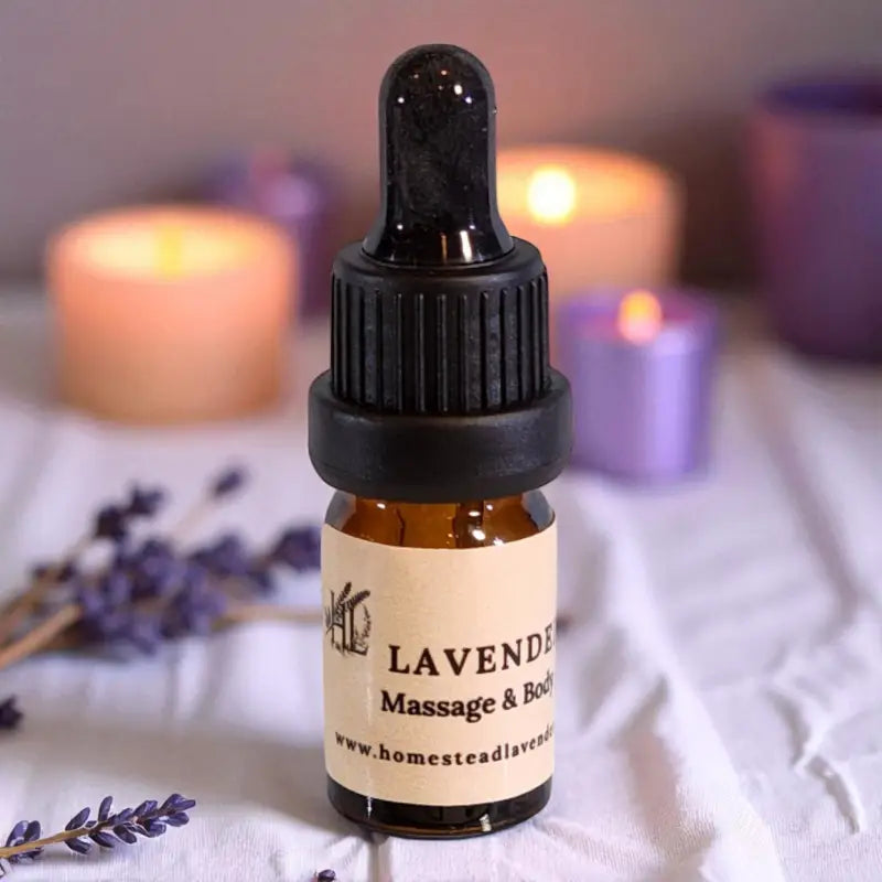 Dropper bottle of lavender massage oil with candles and sprigs of lavender