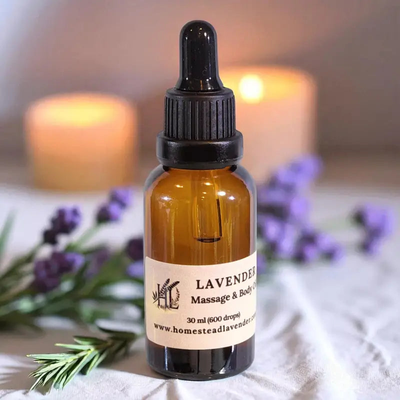 A 30ml dropper bottle of lavender massage oil with candles and sprigs of lavender