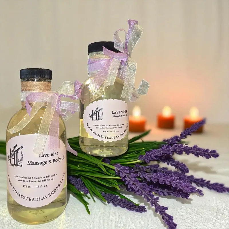 A 8 & 16 fl. oz. clear glass bottle of lavender massage oil with candles and sprigs of lavender