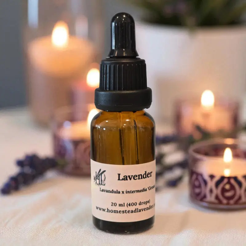 Amber bottle of lavender essential oil (20ml) with a dropper on a table, surrounded by fresh lavender and a glowing candle.