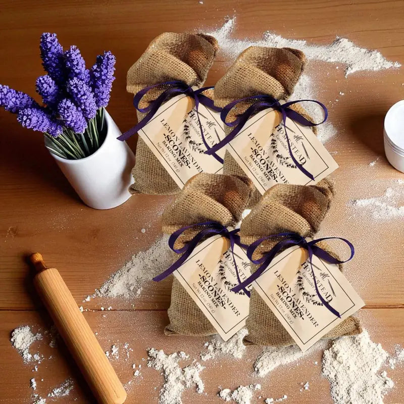 Four bags of Lemon Lavender Scones Mix tied with purple ribbon, surrounded by baking ingredients and lavender flowers sitting on a light table