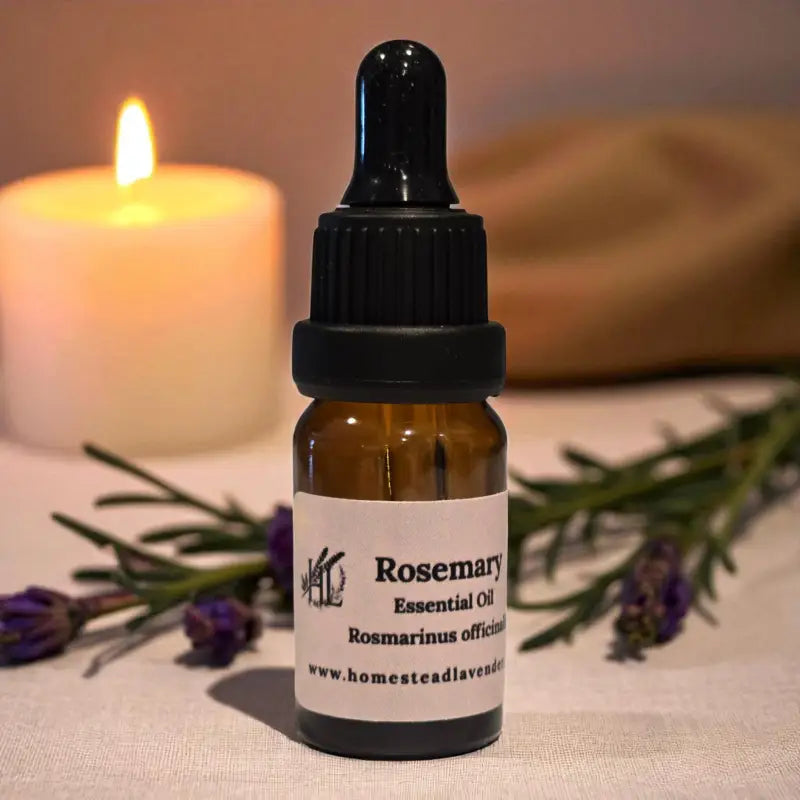 Amber dropper bottle of rosemary essential oil beside candles and lavender – handcrafted on our Homestead Lavender Tennessee farm.