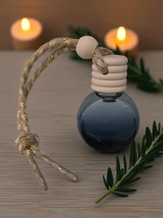 Glass rosemary car diffuser with wooden cap, styled with rosemary sprigs and candles on a light wood surface from Homestead Lavender Farm.