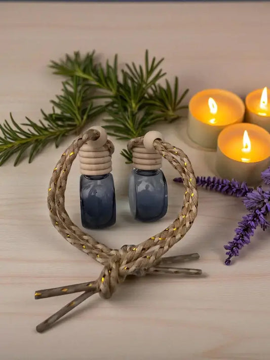 Glass rosemary car diffuser with wooden cap, styled with rosemary sprigs and lavender with candles on a light wood surface from Homestead Lavender Farm.