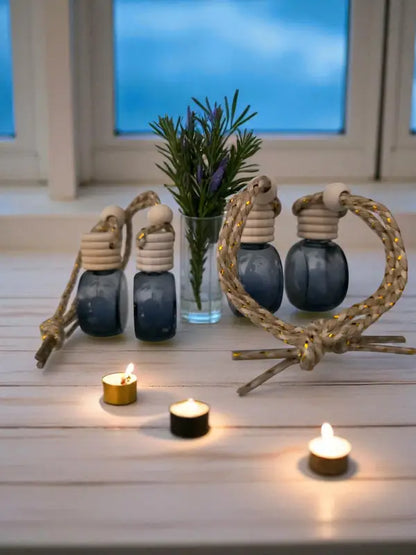 Four glass rosemary car diffuser with wooden cap, styled with rosemary sprigs and lavender with candles on a light wood surface Homestead Lavender Farm.