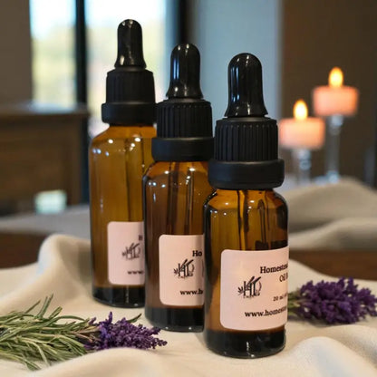 Three amber glass bottles with black dropper lids of massage oil on a cloth with lavender and rosemary, candles in the background.