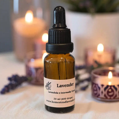 Amber bottle of lavender essential oil (20ml) with a dropper on a table, surrounded by fresh lavender and a glowing candle.
