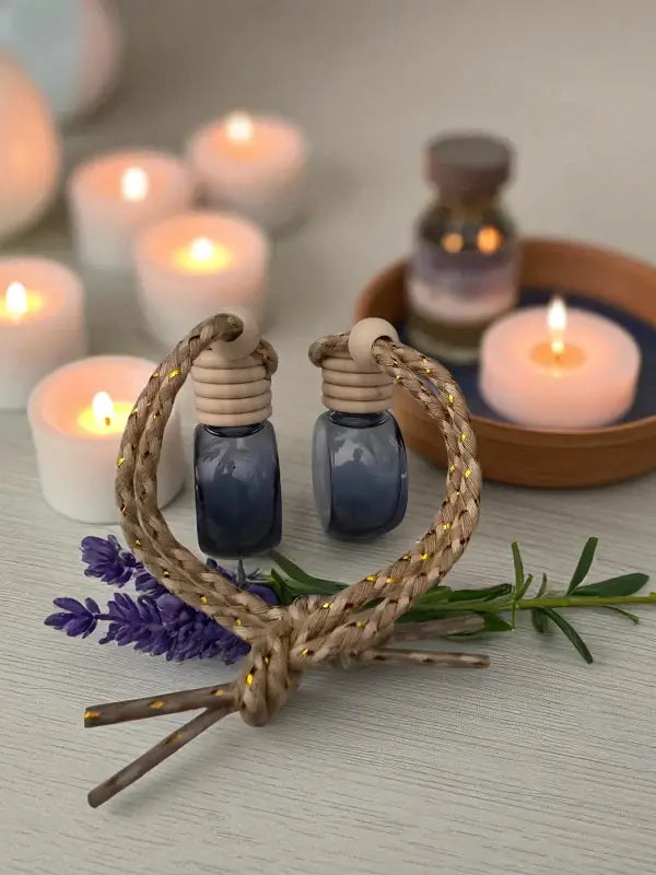 Two glass lavender car diffuser bottle with wooden top and rope, styled with rosemary sprigs and lavender with candles on a light wood surface created at Homestead Lavender Farm.