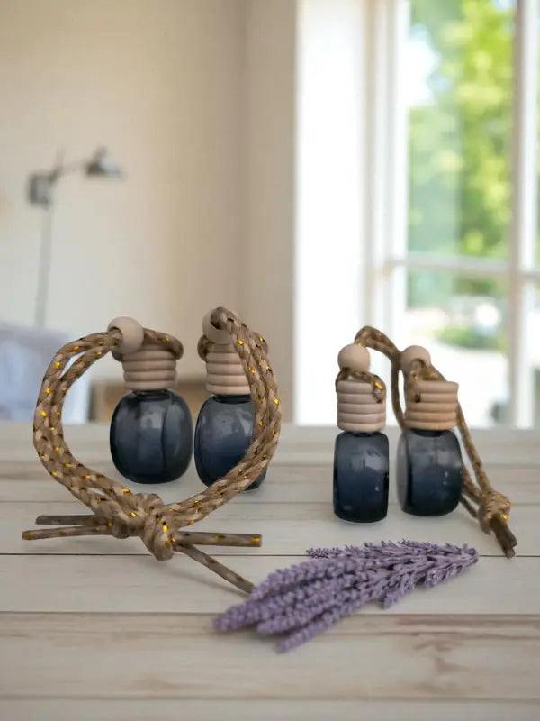 Two glass lavender car diffuser bottle with wooden top and rope, styled with lavender flowers and candles on a light wood surface, created at Homestead Lavender Farm.