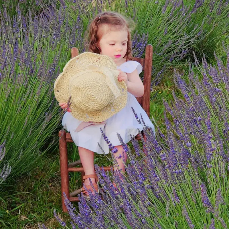 Young girl sitting in a blooming lavender field at Homestead Lavender Farm, holding a sunhat, first photography session on the farm.