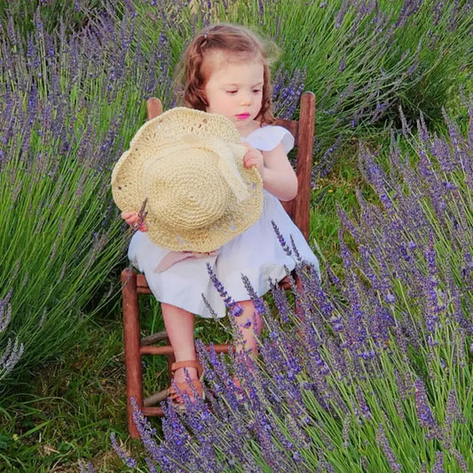 Young girl sitting in a blooming lavender field at Homestead Lavender Farm, holding a sunhat, first photography session on the farm.