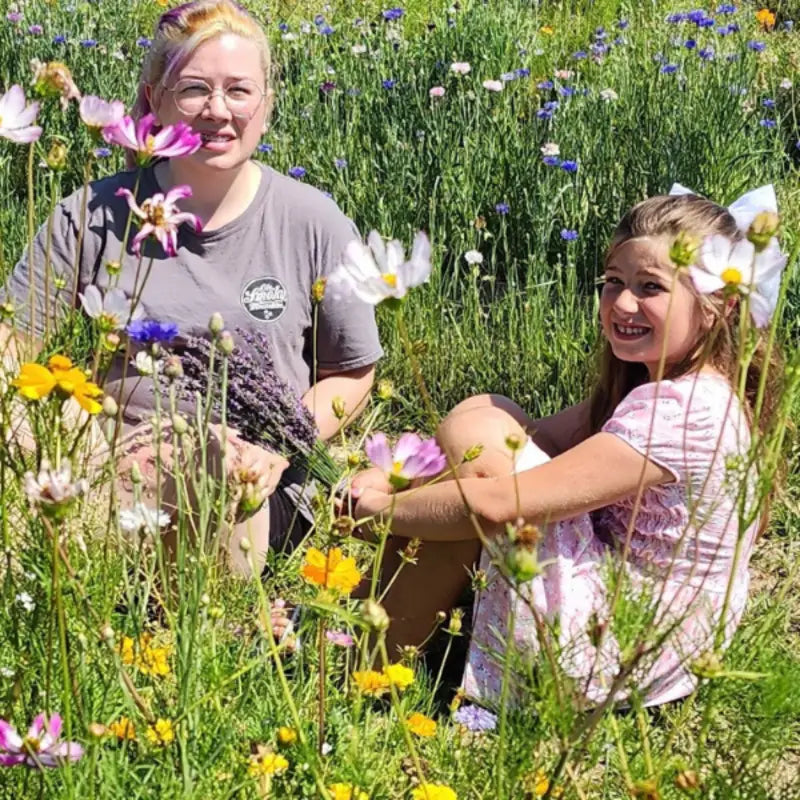 A woman with her child sitting in the wild flowers in bloom between lavender rows on Homestead Lavender Farm.