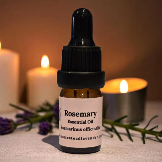 Amber dropper bottle of rosemary essential oil beside candles and lavender – handcrafted on our Homestead Lavender Tennessee farm.