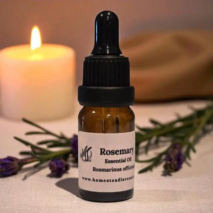 Amber dropper bottle of rosemary essential oil beside candles and lavender – handcrafted on our Homestead Lavender Tennessee farm.